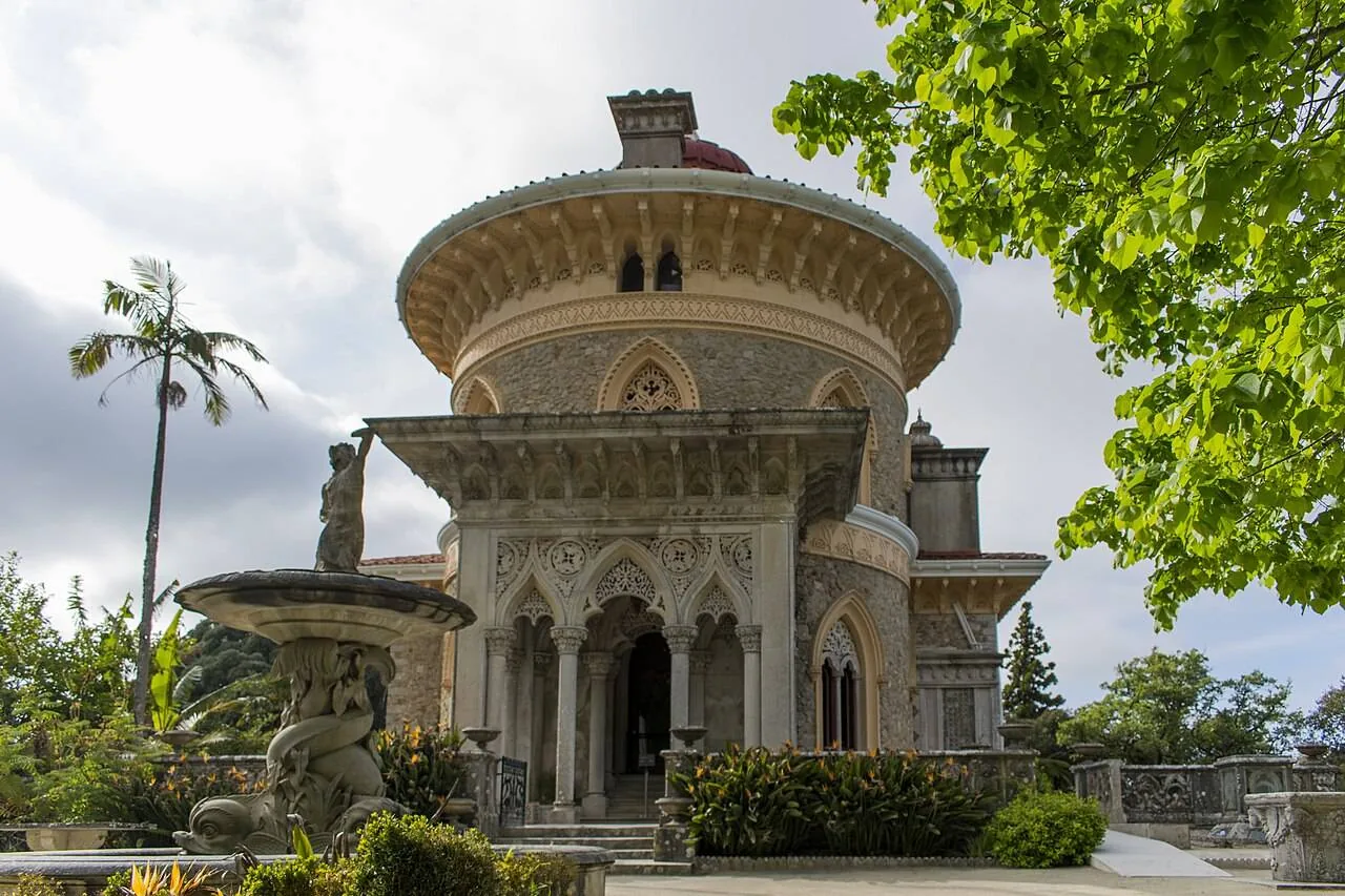 The front of the palace under a grey sky, its round pavilion and arcaded porch above a stone fountain
