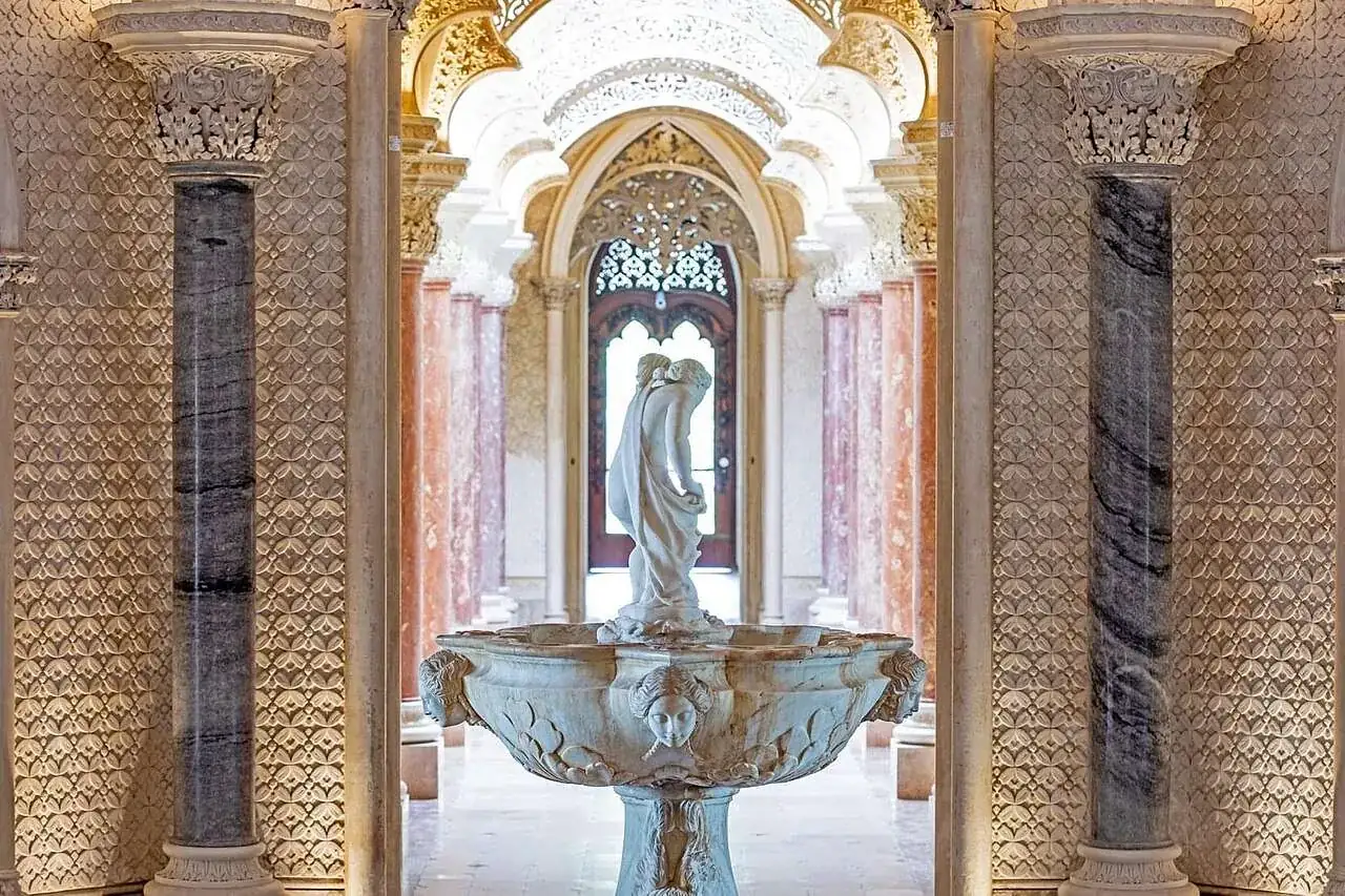 The central hall: a marble fountain with a standing figure, framed by two polished columns under carved and pierced plasterwork